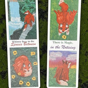 May include: Two rectangular bookmarks featuring painted fox illustrations. The left bookmark shows a fox by a waterfall and curled up in flowers with the text "Whimsy lives in the Spaces Between". The right shows a fox and sunset with "There is Magic, in the Noticing".