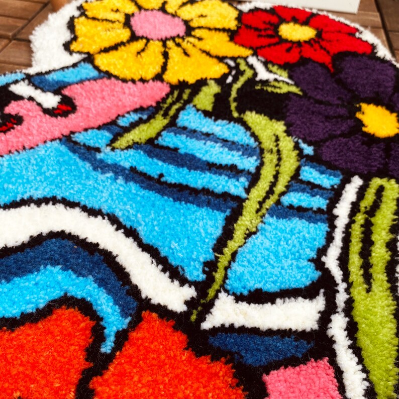 Może przedstawiać: Kolorowy dywan z kwiatowym wzorem. Dywan przedstawia duży ż&oacute;łty kwiat z czerwonymi i białymi akcentami, mniejszy czerwony kwiat z białymi akcentami i fioletowy kwiat z białymi akcentami. Dywan ma r&oacute;wnież wz&oacute;r w niebieskie i białe pasy.