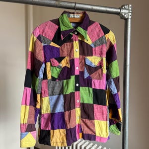 May include: A patchwork long-sleeve shirt with a button-up front. The shirt is made of different colored fabrics, including pink, purple, yellow, green, and black.