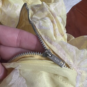 May include: Close-up of a yellow fabric zipper with a silver zipper pull. The zipper pull has the word "ONDA" printed on it.