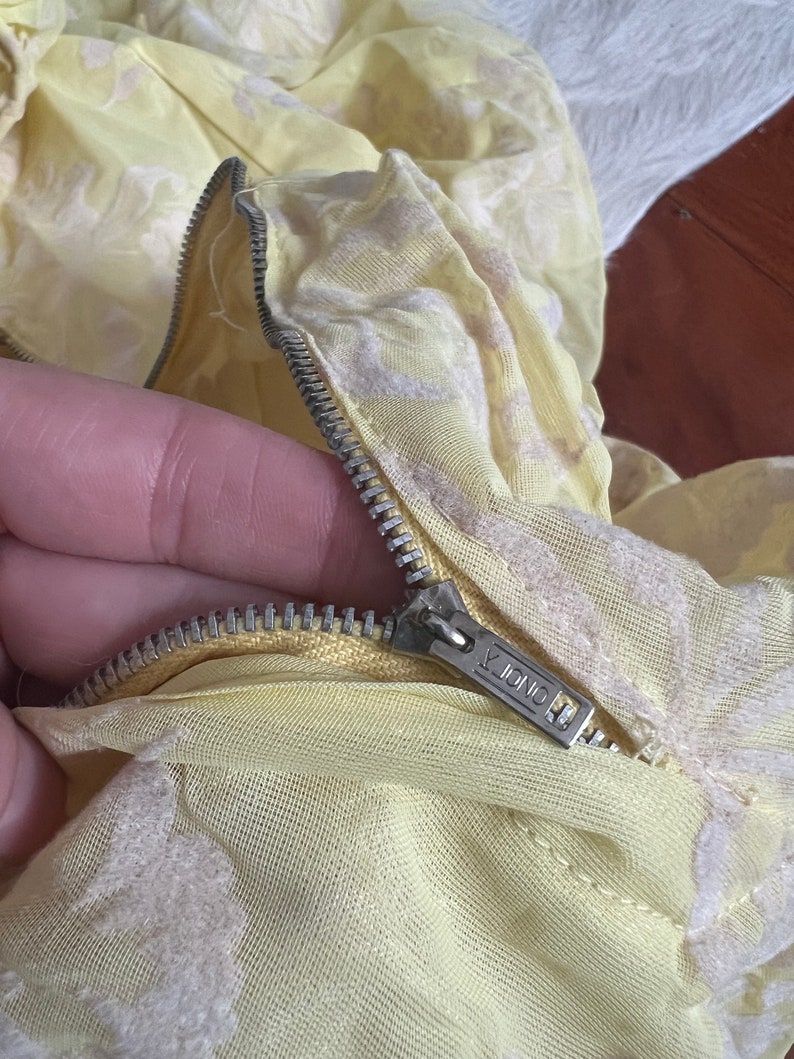 May include: Close-up of a yellow fabric zipper with a silver zipper pull. The zipper pull has the word "ONDA" printed on it.