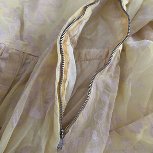 May include: A yellow dress with a white floral pattern and a zipper closure. The zipper is visible and open, showing the inside of the dress.