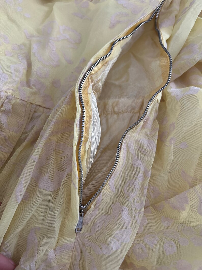 May include: A yellow dress with a white floral pattern and a zipper closure. The zipper is visible and open, showing the inside of the dress.