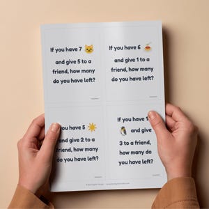 Può includere: Una scheda bianca con quattro problemi di sottrazione, ognuno con una domanda e illustrazioni. La scheda è tenuta in mano su uno sfondo beige. Il testo include domande come "Se hai 7 e ne dai 5 a un amico, quanti te ne rimangono?"