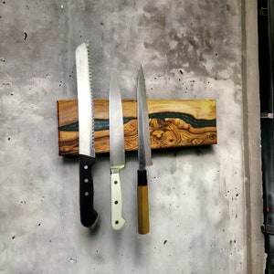 May include: Three kitchen knives are mounted on a wooden magnetic knife holder with a green epoxy resin inlay. The holder is attached to a gray wall.