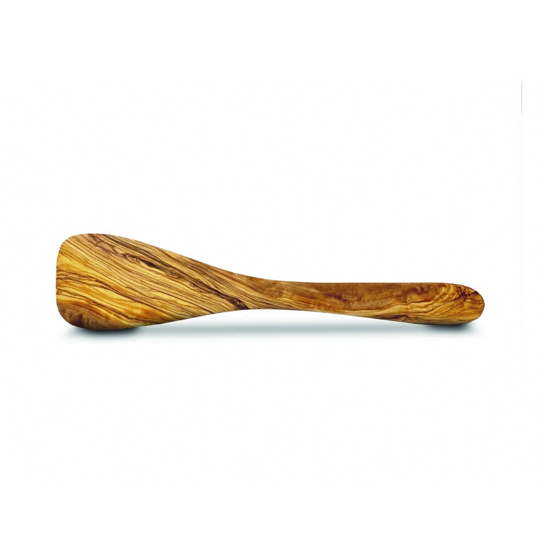 Puede incluir: Una esp&aacute;tula larga de madera con una cabeza redondeada ligeramente curvada. La esp&aacute;tula est&aacute; hecha de madera de olivo y tiene un color natural marr&oacute;n claro con patrones de grano marr&oacute;n oscuro.