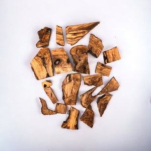 May include: A collection of irregularly shaped pieces of olive wood, with a natural brown and dark brown color, arranged in a heart shape on a white background.
