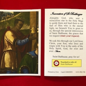 May include: A religious card with a painting of a man holding a golden chalice. The card has text that reads "Invocation of St Balthazar" and "Touched to relic of: Saint Balthazar".