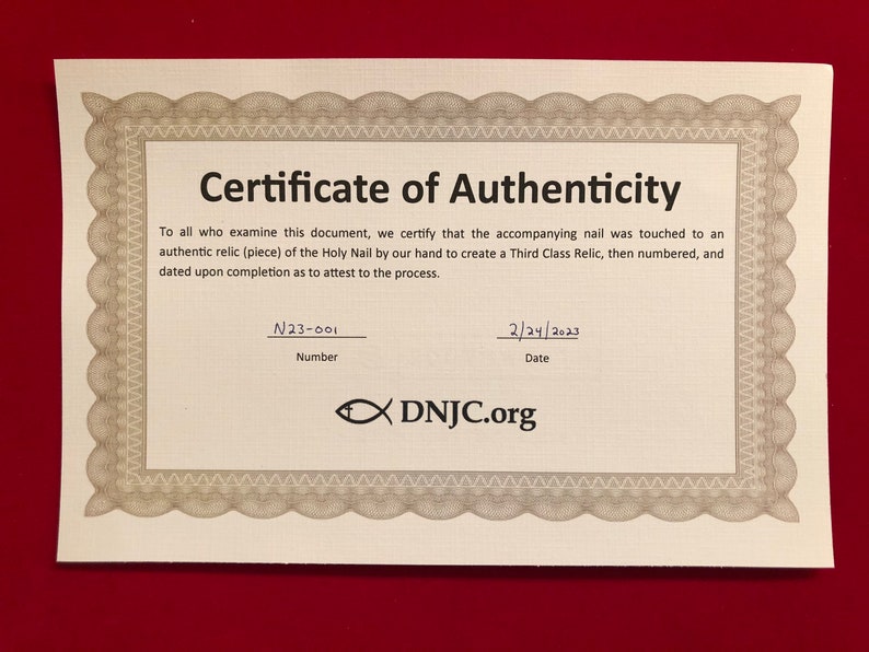 May include: A certificate of authenticity with a decorative border. The certificate states that the accompanying nail was touched to an authentic relic of the Holy Nail. The certificate is numbered N23-001 and dated 2/24/2023. The certificate is from DNJC.org.