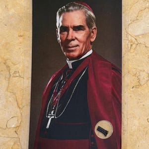 Könnte beinhalten: Eine rechteckige Gebetskarte mit dem Porträt eines Bischofs, der ein rotes Zucchetto, eine rote Mozetta über einer schwarzen Soutane und ein silbernes Brustkreuz an einer Kette trägt. Eine kleine Reliquienkapsel ist unten rechts eingelassen.