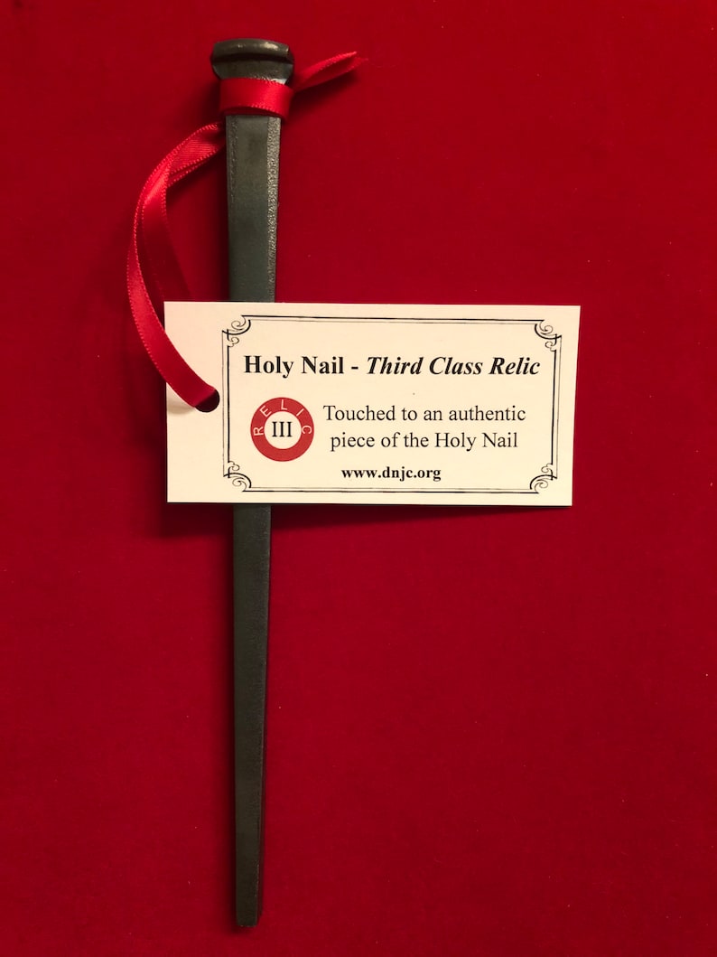 May include: A black metal nail with a red ribbon tied around the top. A white card with black text reads "Holy Nail - Third Class Relic" and "Touched to an authentic piece of the Holy Nail" and "www.dnjc.org".
