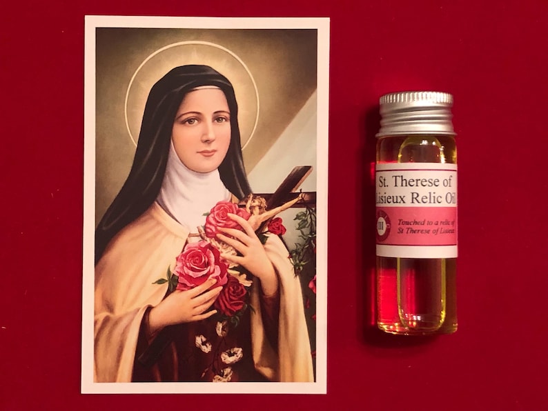 Puede incluir: Una botella de aceite de reliquia religiosa con una etiqueta que dice "St. Therese of Lisieux Relic Oil" y "Touched to a relic of St. Therese of Lisieux". La botella es transparente y contiene un l&iacute;quido amarillo. La botella est&aacute; al lado de una imagen de Santa Teresa de Lisieux, una santa cat&oacute;lica, sosteniendo un ramo de rosas.
