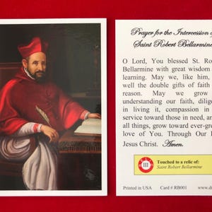May include: A prayer card featuring a portrait of Saint Robert Bellarmine, a Catholic saint, dressed in red robes. The card includes a prayer for his intercession and a note indicating that it has been touched to a relic of the saint. The text on the card reads: "Prayer for the Intercession of Saint Robert Bellarmine. O Lord, You blessed St. Robert Bellarmine with great wisdom and learning. May we, like him, use well the double gifts of faith and reason. May we grow in understanding our faith, diligence in living it, compassion in our service toward those in need, and in all things, grow toward ever-greater love of You. Through Our Lord Jesus Christ. Amen. Touched to a relic of: Saint Robert Bellarmine. Printed in USA Card # RB001 www.dnjc.org"