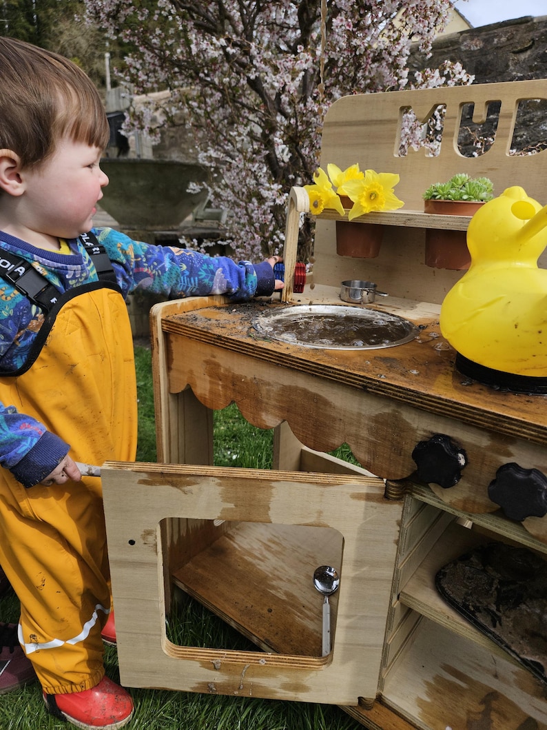 Stylish scalloped mud kitchen with four ring hob, four dials,two stainless steel sinks, two taps with hot and cold handles andwith full oven and shelf