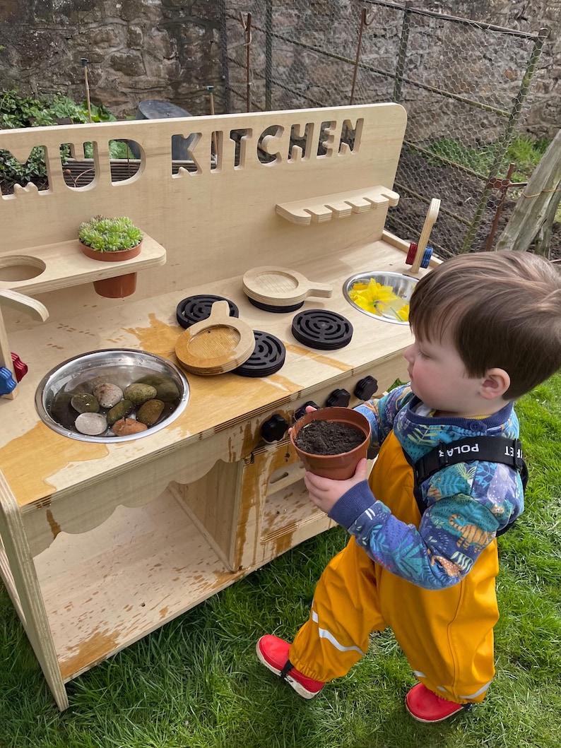 small boy playing with mud in his mud kitchen sink, outdoor play