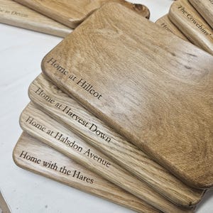 K&ouml;nnte beinhalten: Eine Reihe von Holzschneidebrettern mit Gravuren. Die Bretter sind hellbraun und zeigen eine deutliche Holzmaserung. Texte umfassen "Home at Hillcot", "Home at Harvest Down", "Home at Halsdon Avenue" und "Home with the Hares".