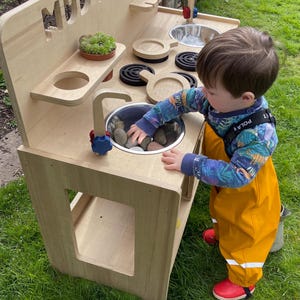 small boy playing with rocks in his mud kitchen sink