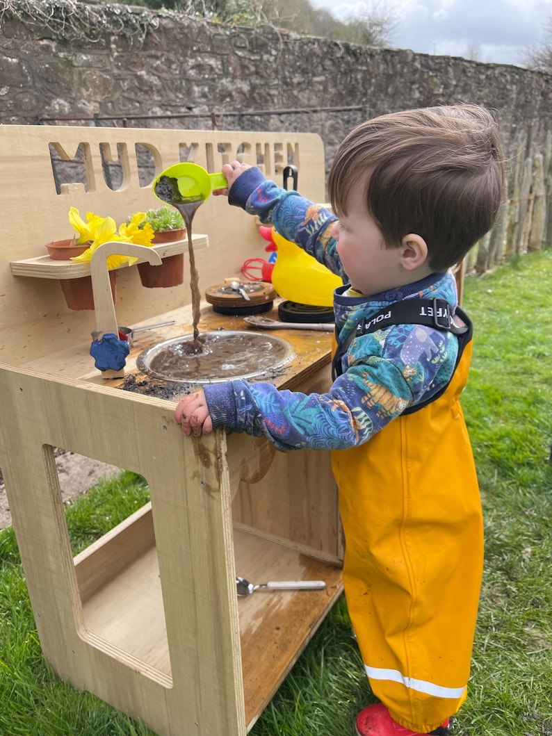 small boy playing mudpies in his mud kitchen sink