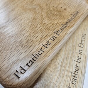 K&ouml;nnte beinhalten: Zwei helle Holzschneidebretter mit den eingravierten Texten "I'd rather be in Pembrokeshire" und "I'd rather be in Devon". Die Bretter haben eine nat&uuml;rliche Holzmaserung.