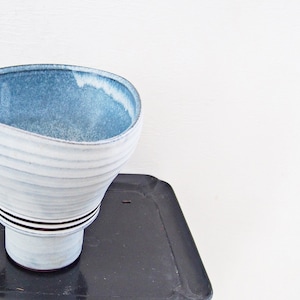 以下が含まれることがあります： 青い釉薬が施された白い陶器の花瓶で、底は茶色です。花瓶は、漏斗や広口のピッチャーに似ており、ユニークな形をしています。花瓶の底には、日本の文字が書かれた茶色のスタンプがあります。