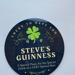 May include: A black and green round sign with the text "LUCKY TO HAVE YOU" and "STEVE'S GUINNESS" in a white font. The sign also includes a green four-leaf clover and the text "A Special Place, for the Special Drink of a VERY Special Man".