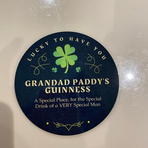 May include: A round, blue and green coaster with the text "Lucky to have you" and "Grandad Paddy's Guinness" with a shamrock design. The text below reads "A Special Place, for the Special Drink of a VERY Special Man."
