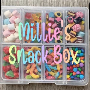 May include: A clear plastic snack box divided into eight sections, each containing a different type of sweet treat. The box is labelled "Millie's Snack Box" in iridescent lettering. Contents include marshmallows, gummy sweets, and chocolate beans.