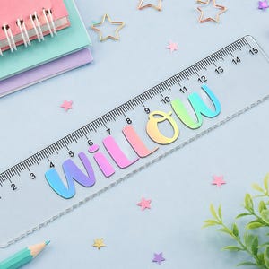 May include: A clear plastic ruler measuring 15 centimetres in length, featuring the name Willow in a colourful, gradient-style font. The ruler includes black measurement markings along the top edge, with numbers ranging from 0 to 15 centimetres.