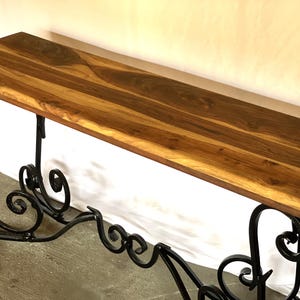 May include: A wooden console table with a natural wood grain top and ornate black wrought iron legs. The table's top is a warm brown color, and the legs feature decorative scrollwork. This piece is suitable for entryways or living rooms.