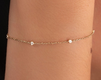 May include: A delicate gold chain bracelet with four small, clear gemstones.