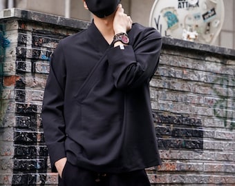 May include: A black long-sleeved shirt with a V-neck and a diagonal fold detail. The shirt is worn by a person with a black face mask and a watch on their wrist.