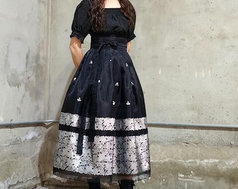 May include: A black dress with a square neckline and short sleeves. The skirt features a silver and white floral pattern at the hem and scattered across the black fabric. The dress is paired with black boots.