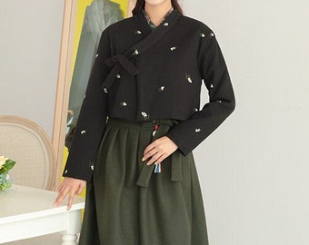 May include: A black long-sleeved top with white floral embroidery and a wrap-style closure, paired with a long olive green skirt. The outfit is a traditional Korean design, with a modern silhouette.