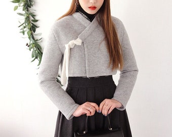 May include: A gray cropped jacket with a white tie detail, worn with a black beret, black skirt, and a black handbag.