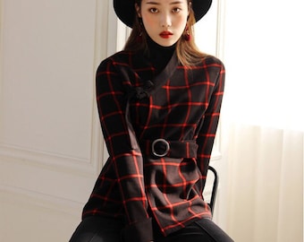 May include: A black and red plaid jacket with a matching belt and a black hat. The jacket has a unique design with a wrap-style front and a belt with a silver buckle. The outfit is completed with black pants.