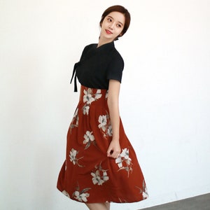 May include: A woman wearing a black short-sleeved top with a tied neckline and a rust-colored skirt with white floral print.