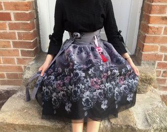May include: A black and gray floral skirt with a black top and a red tassel. The skirt is made of a sheer fabric and has a flowing silhouette.