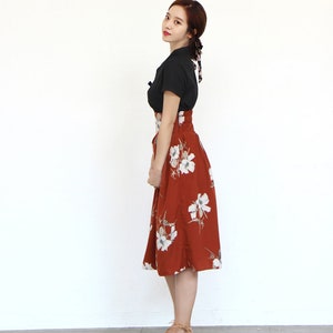 May include: A woman wearing a black short-sleeved top and a rust-colored skirt with white floral print. The skirt has a high waist and a slightly flared silhouette.