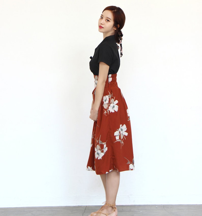 May include: A woman wearing a black short-sleeved top and a rust-colored skirt with white floral print. The skirt has a high waist and a slightly flared silhouette.