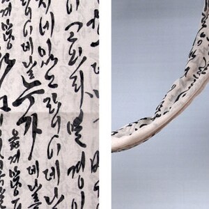 May include: A white fabric scarf with black calligraphy writing. The scarf is hanging in a curved shape.