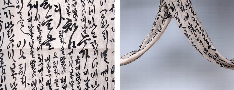 May include: A white fabric scarf with black calligraphy writing. The scarf is hanging in a curved shape.