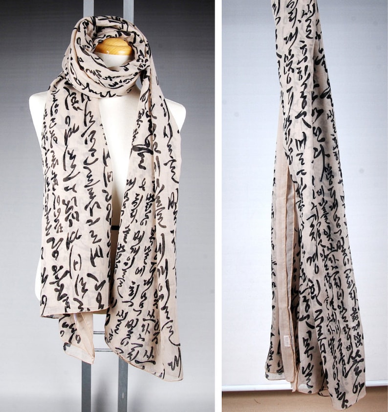 May include: A beige scarf with black calligraphy-style writing all over it. The scarf is draped over a mannequin.