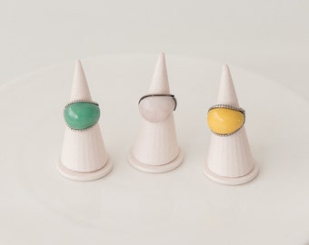May include: Three rings with oval-shaped stones set in silver. The stones are green, white, and yellow.