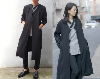 May include: Two people wearing long black coats with a contrasting gray inner lining. The coats have a shawl collar and are open in the front. The people are wearing black pants and shoes.