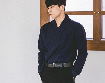 May include: A navy blue wrap-style top with long sleeves, paired with black pants and a black belt. The outfit is simple and elegant, suitable for various occasions. The background includes a window.
