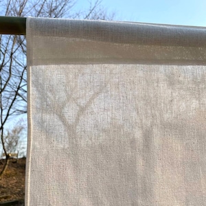 May include: A white cotton fabric hanging on a wooden rod. The fabric is thin and translucent, allowing light to pass through it.