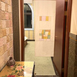 May include: A hallway with a wooden door, a tiled wall with a geometric pattern, and a stone wall with a small vase on a table.