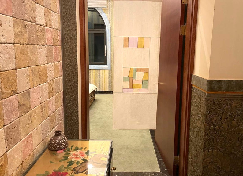 May include: A hallway with a wooden door, a tiled wall with a geometric pattern, and a stone wall with a small vase on a table.