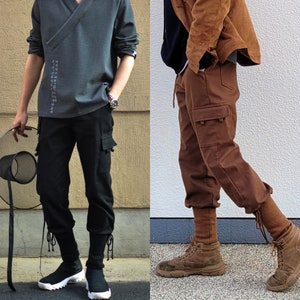 Könnte beinhalten: Zwei Männer tragen verschiedene Arten von Cargohosen. Der Mann links trägt ein dunkelgraues Langarmshirt mit schwarzen Cargohosen und schwarzen Turnschuhen. Der Mann rechts trägt eine braune Jacke mit braunen Cargohosen und braunen Stiefeln.