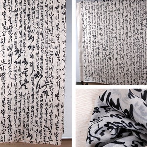 May include: A white fabric scarf with black calligraphy printed on it. The scarf is folded and draped over a surface. The calligraphy is in Korean.